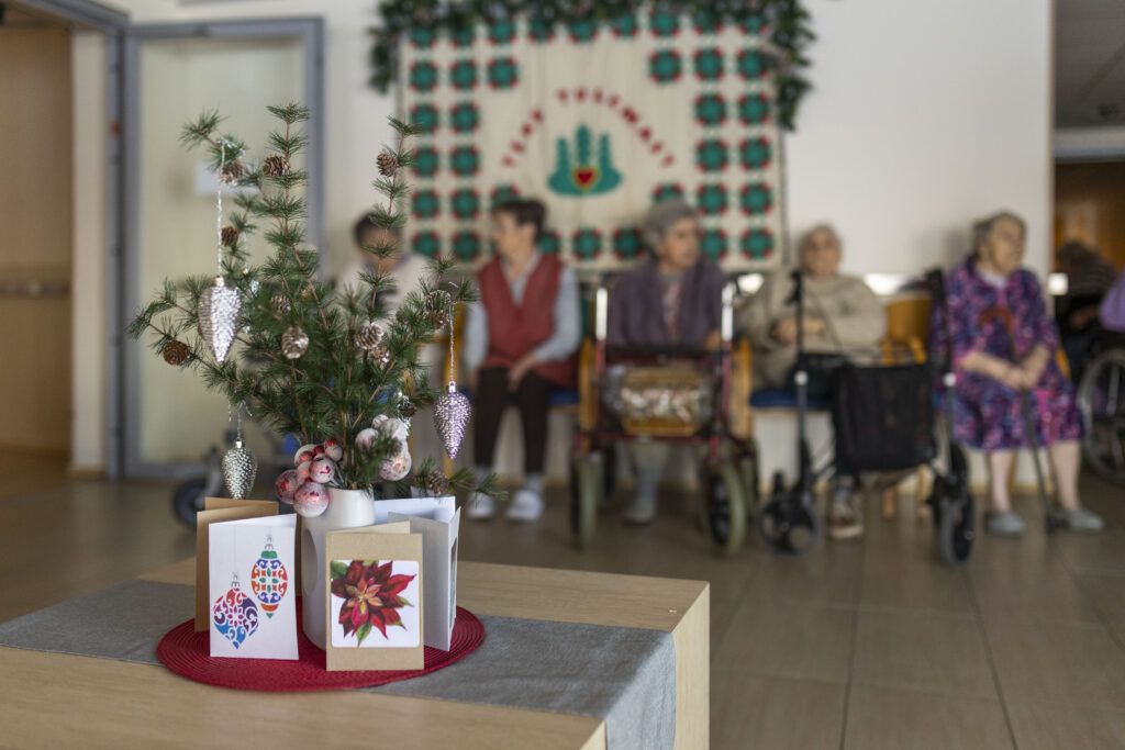 Alutaguse Hoolekeskuse eakad jõuluehtes toas, esiplaanil kuuseoks ja jõulukaardid.